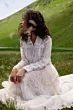 Abito boho bianco in pizzo su donna seduta in prato verde, sfondo collinare.