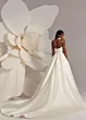 Abito da sposa elegante Dallas di Eva Lendel, con schiena scoperta e lunga gonna, accanto a un grande fiore bianco.