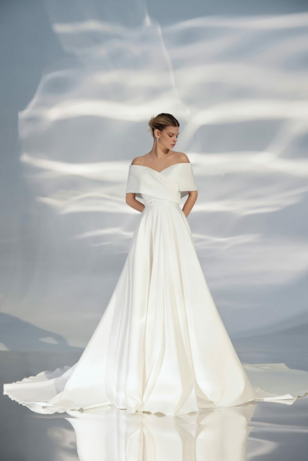 Abito da sposa ARIAMO LIGHT L306, elegante e moderno con scollo a barca e gonna ampia, sfondo luminoso.