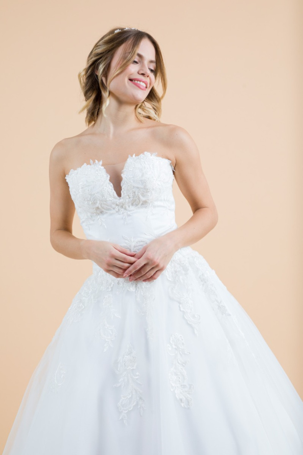 Abito da sposa tulipano bianco con ricami floreali, scollo a cuore, indossato da modella sorridente su sfondo beige.