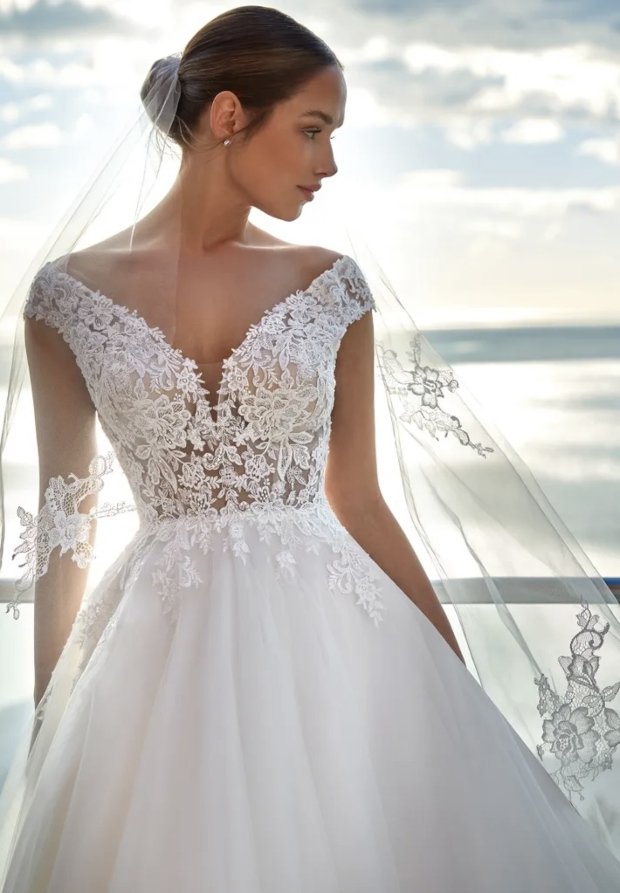 Abito da sposa Sofiane Nicole Jolies in pizzo, scollo a V, sfondo mare al tramonto.
