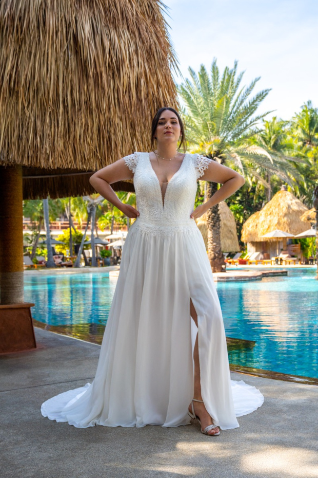 Abito da sposa Bella by Amelie 30113W, scollo a V, pizzo, sfondo tropicale, piscina, atmosfera elegante.