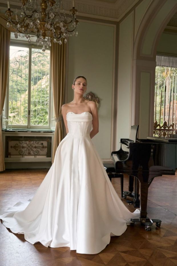 Abito da sposa elegante MILA, The Romantica Collection, in salone classico con pianoforte e lampadario.