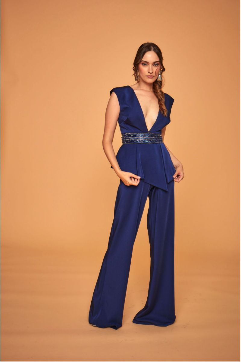 Tuta elegante blu LPA292 Linea Le Preziose, scollo profondo e cintura decorativa, su sfondo beige.