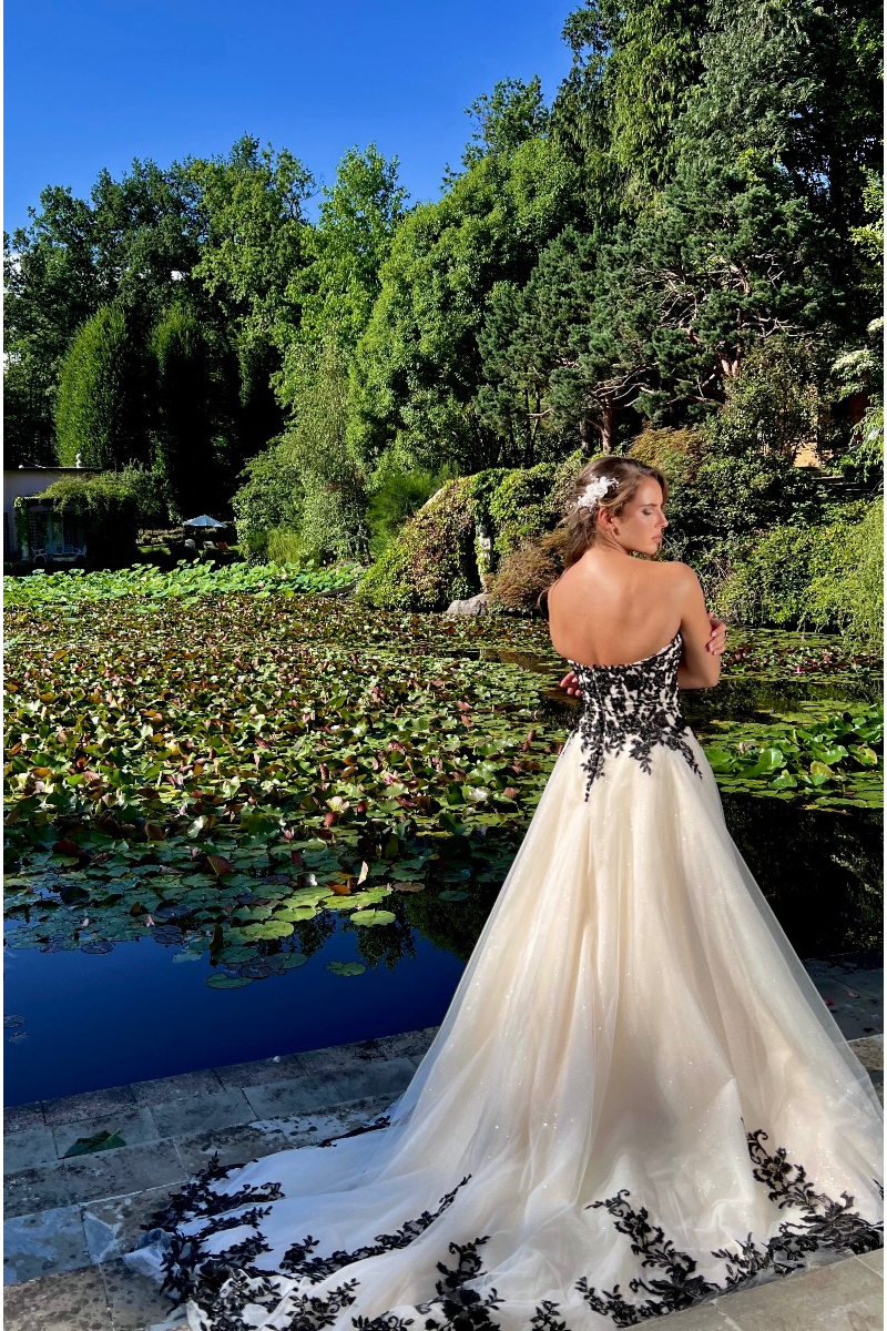 Abito da sposa Eris Linea Sposae Atelier con dettagli neri, sfondo naturale con lago e alberi.