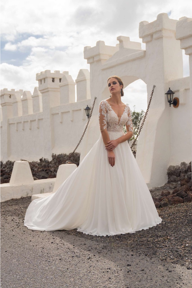 Abito da sposa Amelie 20285 in pizzo e chiffon, sfondo architettura bianca.