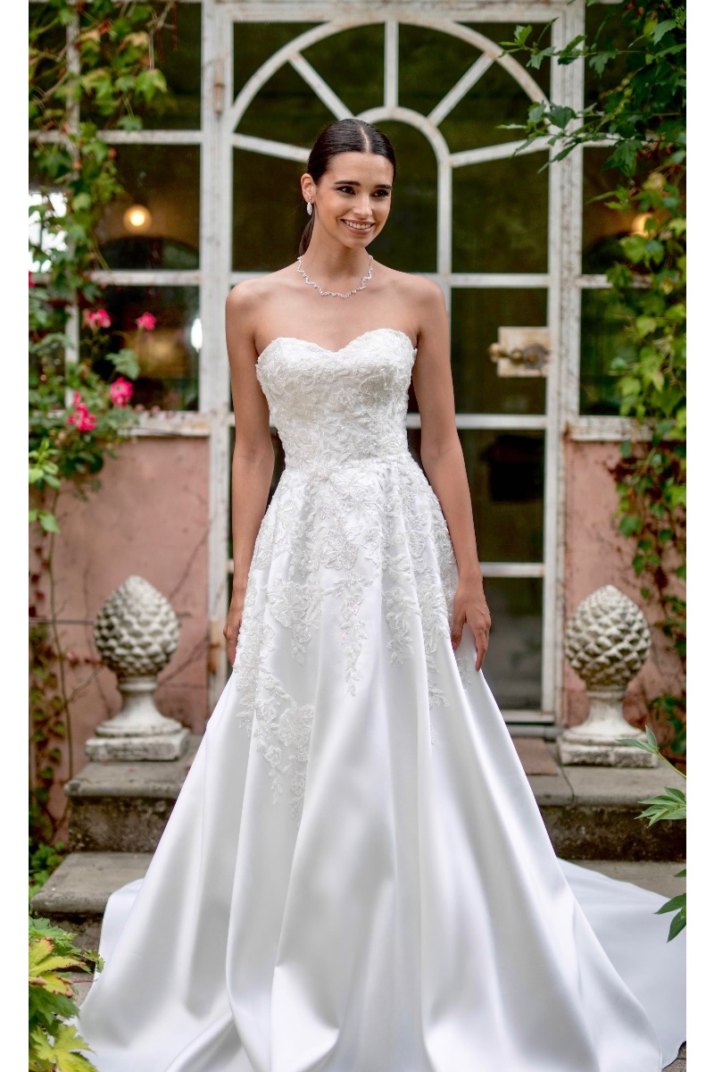 Abito da sposa Antiope in pizzo bianco, scollatura a cuore, ambientato in giardino romantico.