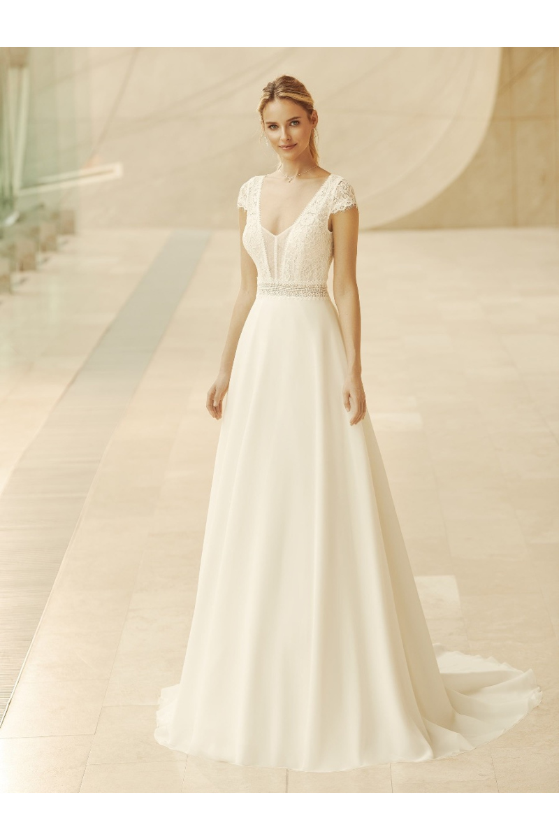Abito da sposa Arleta elegante con corpetto in pizzo e gonna fluida, sfondo moderno.
