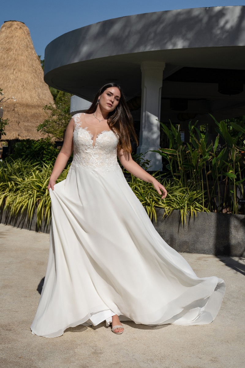 Abito da sposa BELLA BY AMELIE 30108W, elegante e fluente, indossato da modella in giardino soleggiato.