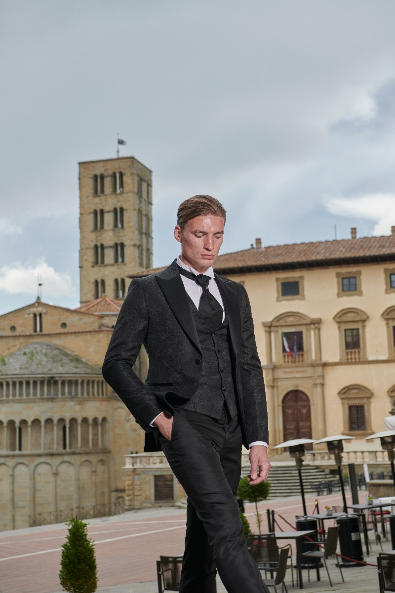 Abito elegante Rocchini 33 indossato da modello in piazza storica, sfondo di edifici antichi e cielo nuvoloso.
