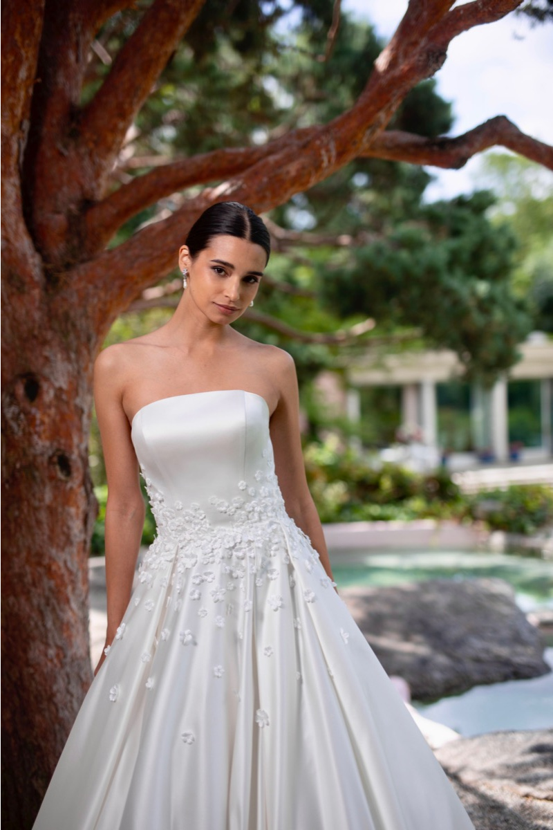 Abito da sposa Monoi linea Sposae Atelier, stile romantico con dettagli floreali, sfondo naturale.