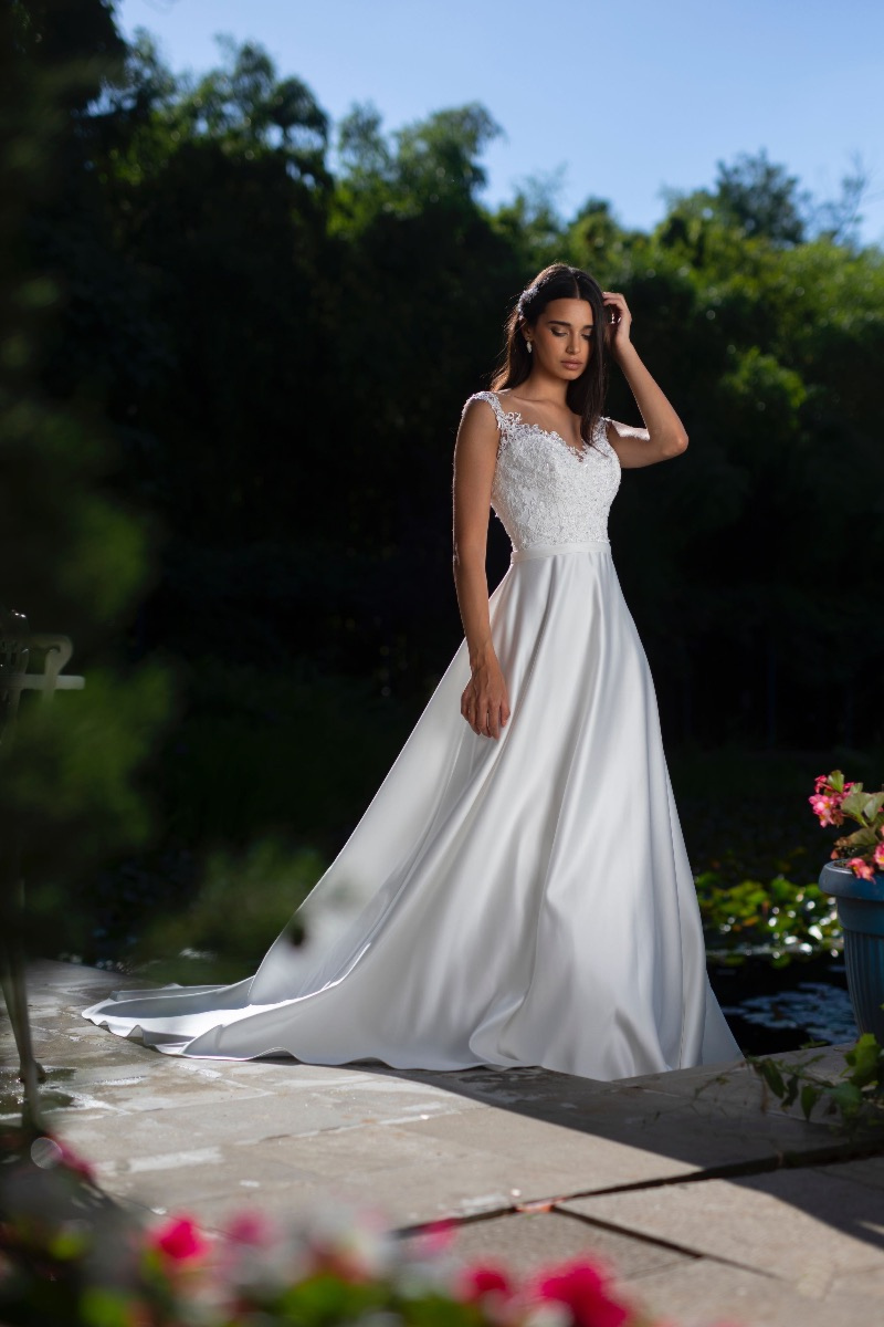 Abito da sposa elegante con corpetto in pizzo e gonna fluente, indossato in un giardino fiorito.