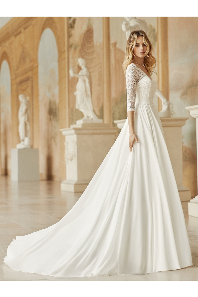 Abito da sposa medusa con pizzo e maniche a tre quarti, sfondo classico con statue e affreschi.
