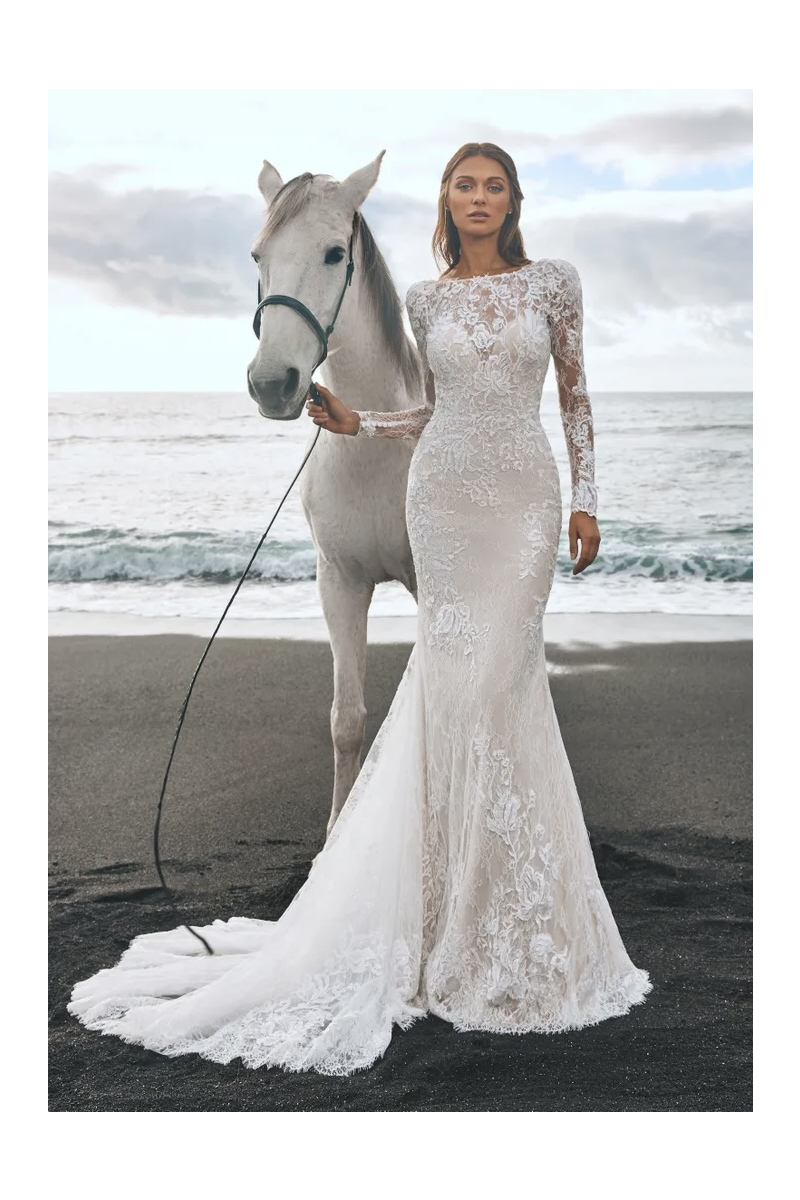 Abito da sposa Pronovias Panjin in pizzo bianco, donna in spiaggia con cavallo bianco sullo sfondo del mare.