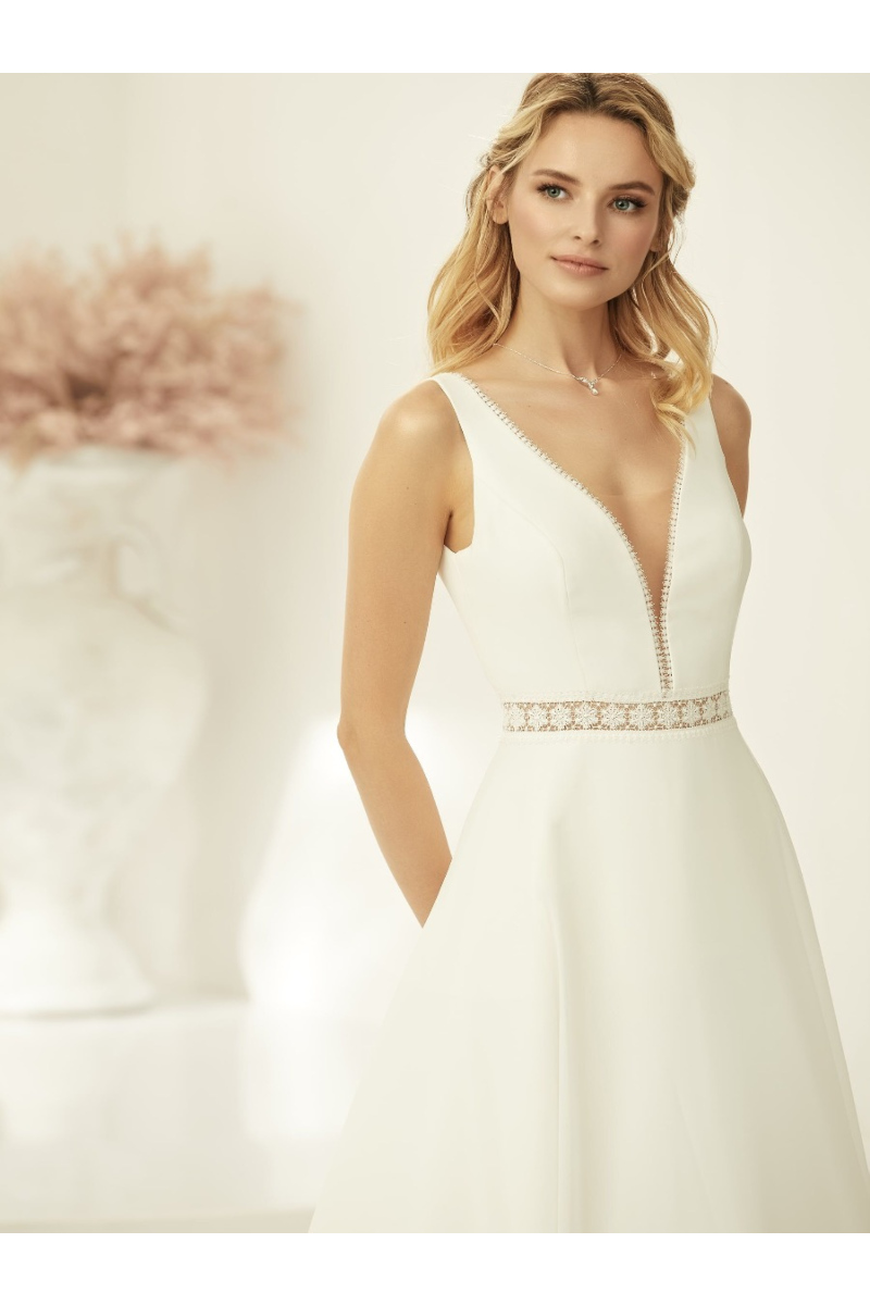 Abito da sposa Azaria con scollo a V e dettagli in pizzo, indossato da una modella bionda in ambiente elegante.