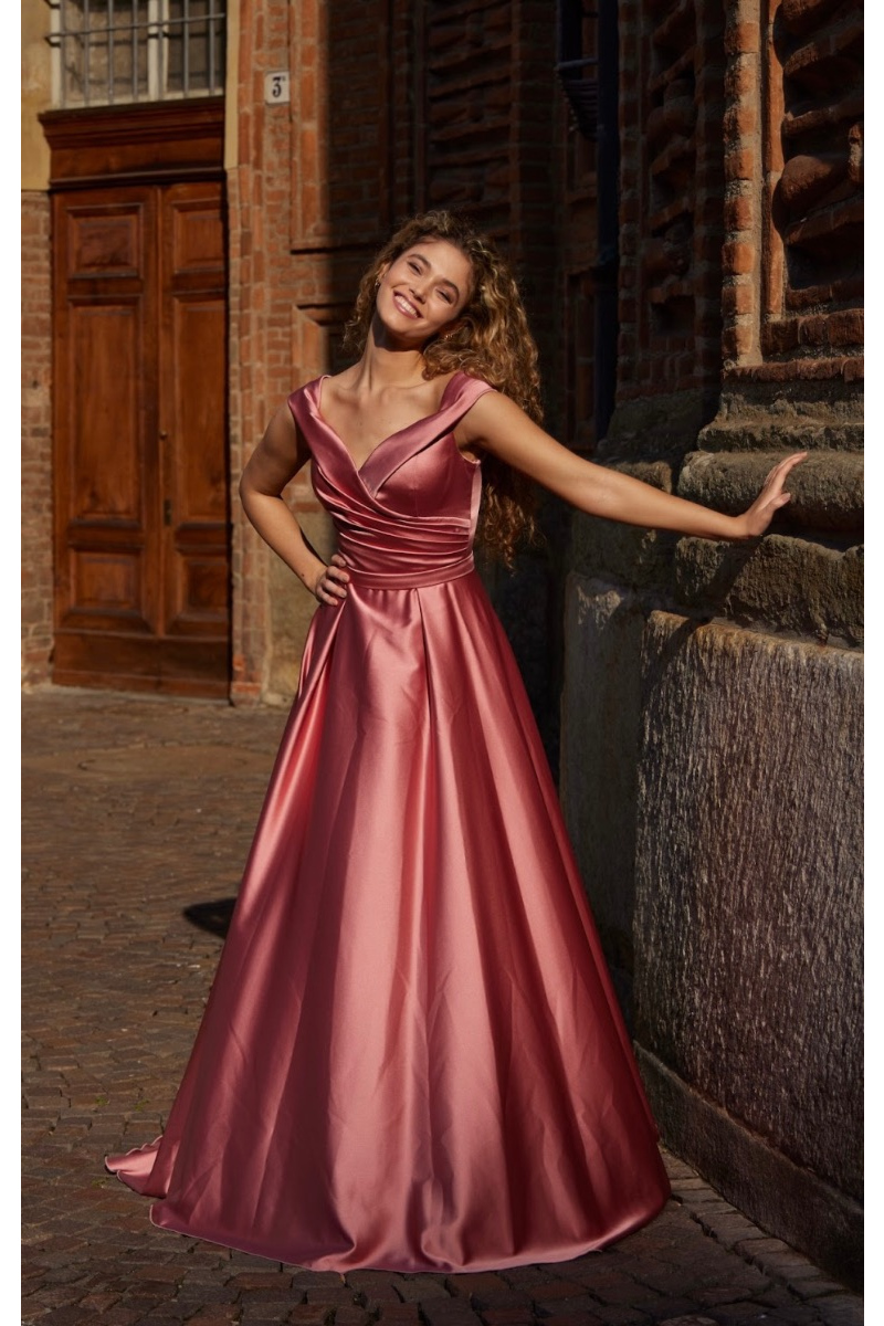 Abito elegante rosa LL50009 Musani, donna sorridente in esterno, sfondo architettonico storico.