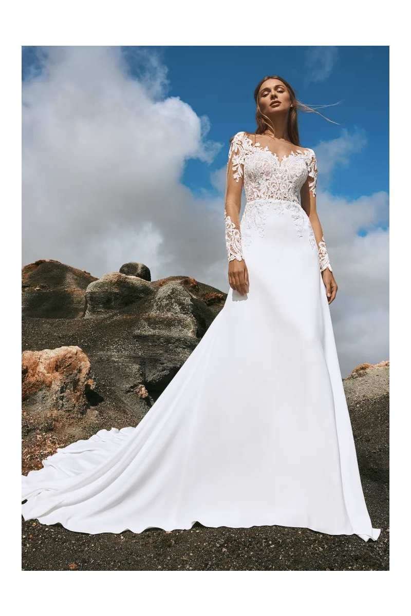 Abito da sposa Pronovias YUSHAN con ricami floreali, sfondo paesaggio roccioso e cielo azzurro.
