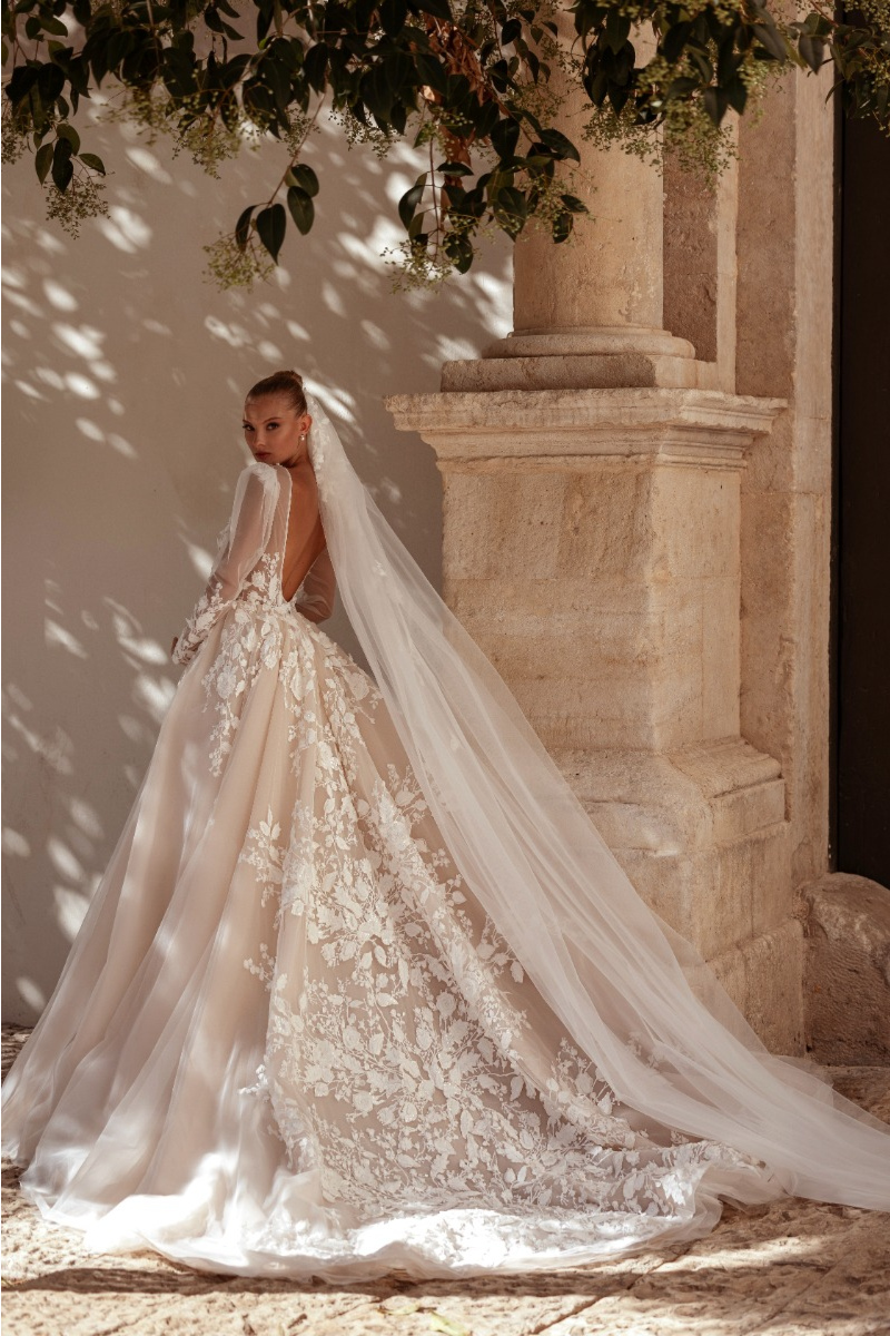 Abito da sposa ACACIA - MADIONI con dettagli floreali e velo lungo, ambientato in un cortile soleggiato.