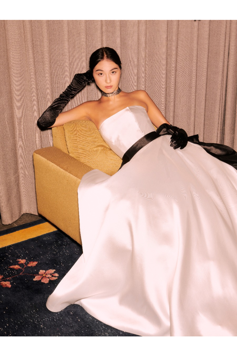 Abito da sposa Marilù Sposae Essential, elegante con guanti neri e cintura, su divano giallo.