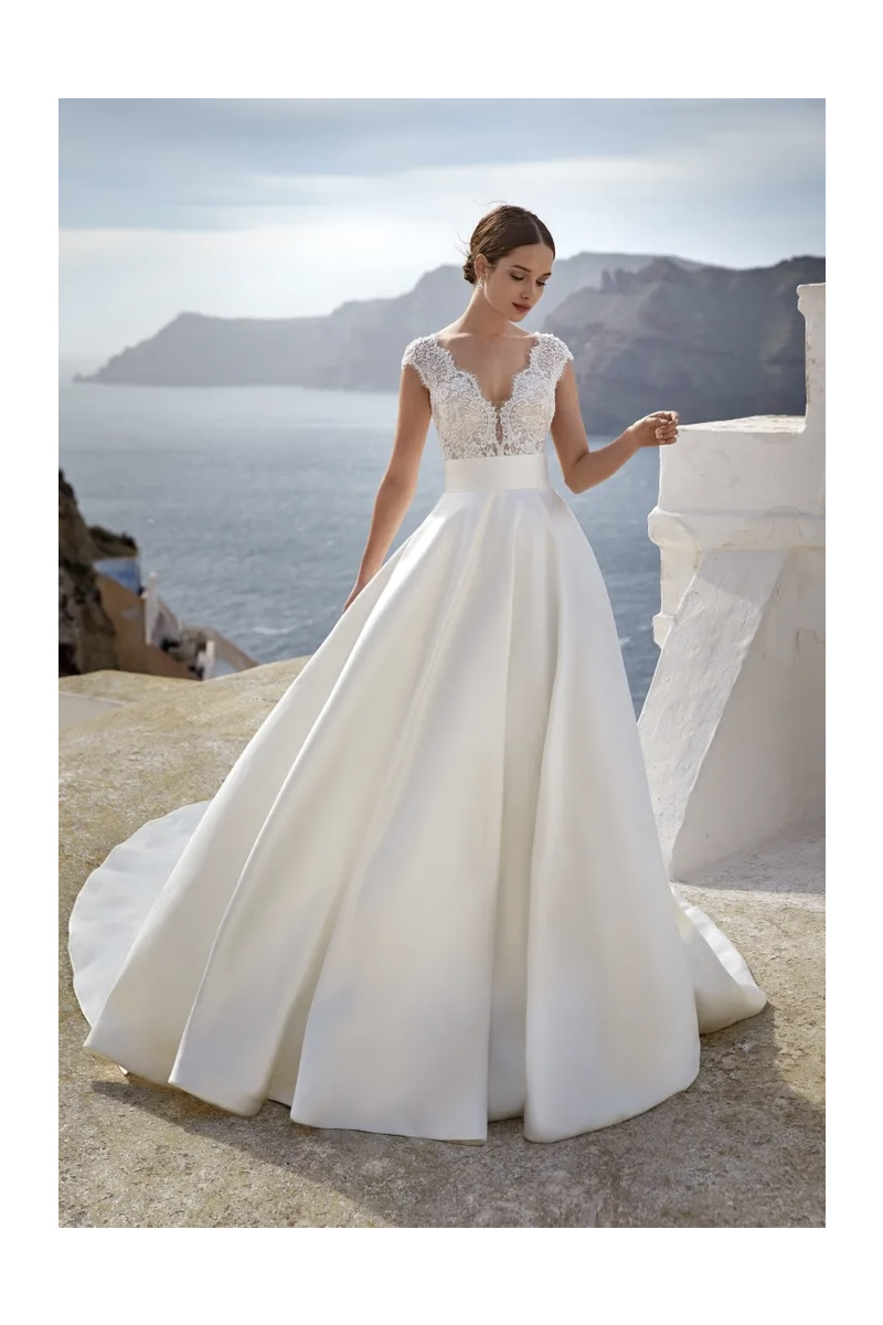 Abito da sposa Favignana Nicole Jolies, scollo a V in pizzo, sfondo mare.