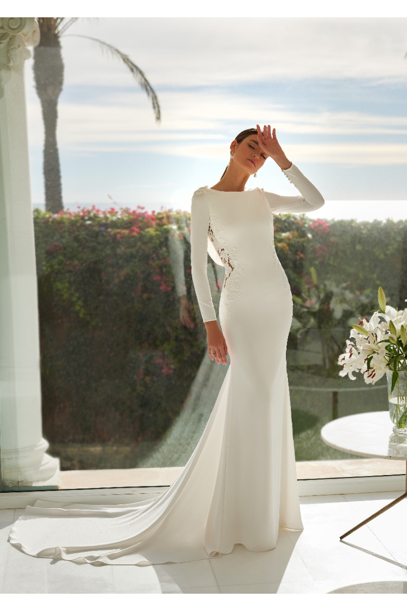 Abito da sposa AELLA St. Patrick, elegante e moderno, con dettagli in pizzo, sfondo floreale e vista panoramica.