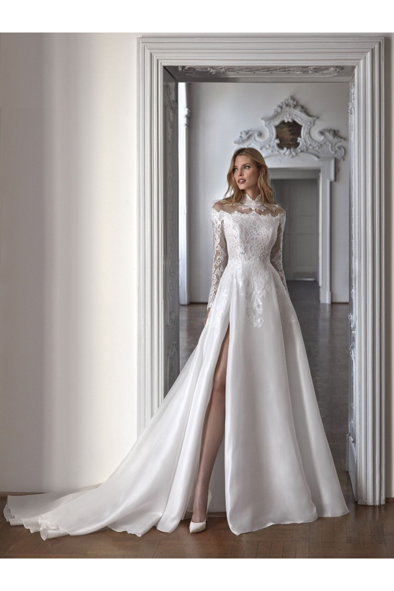Abito da sposa AERIN Nicole Milano in pizzo e seta con spacco, maniche lunghe, sfondo elegante.
