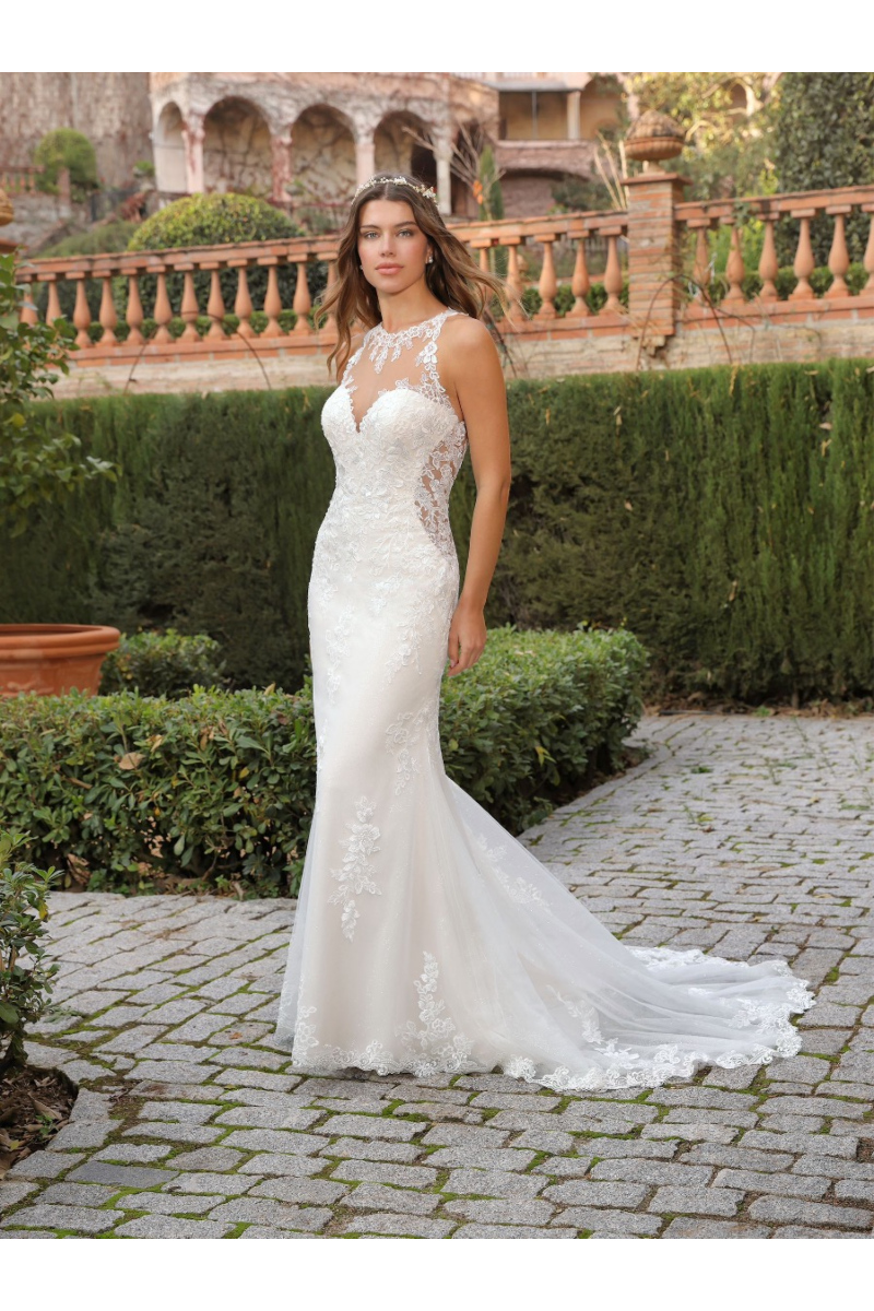 Abito da sposa ALZENA in pizzo bianco, scollatura trasparente, giardino elegante sullo sfondo.