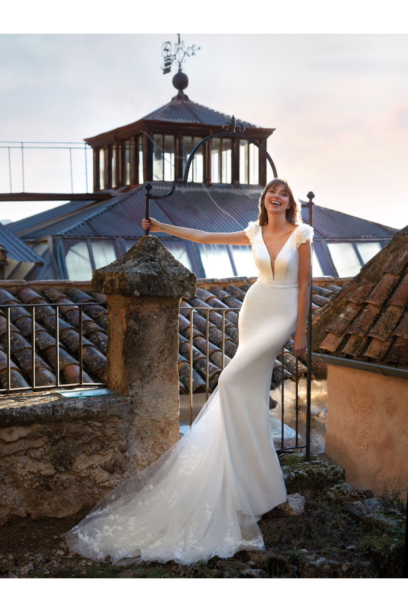 Abito da sposa Nicole Colet AMARANTH, elegante e aderente, con sfondo architettonico suggestivo.