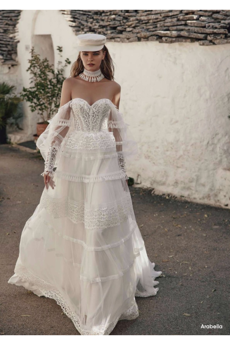 Abito da sposa boho Arabella di Ariamo, con dettagli in pizzo e maniche trasparenti, in ambiente rustico.
