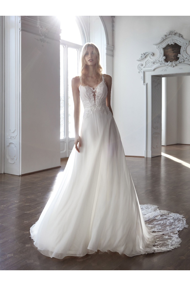 Abito da sposa bianco ARCHES con corpetto in pizzo e gonna fluida in una sala luminosa.