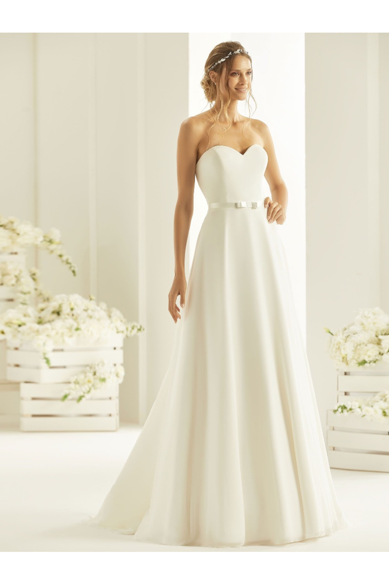 Abito da sposa bianco Harmonia Linea, senza spalline, ambiente elegante con fiori bianchi.