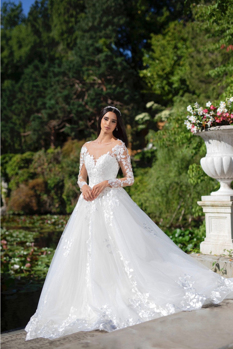 Abito da sposa Asteria Linea Sposae Atelier in giardino, con dettagli floreali e maniche lunghe in pizzo.