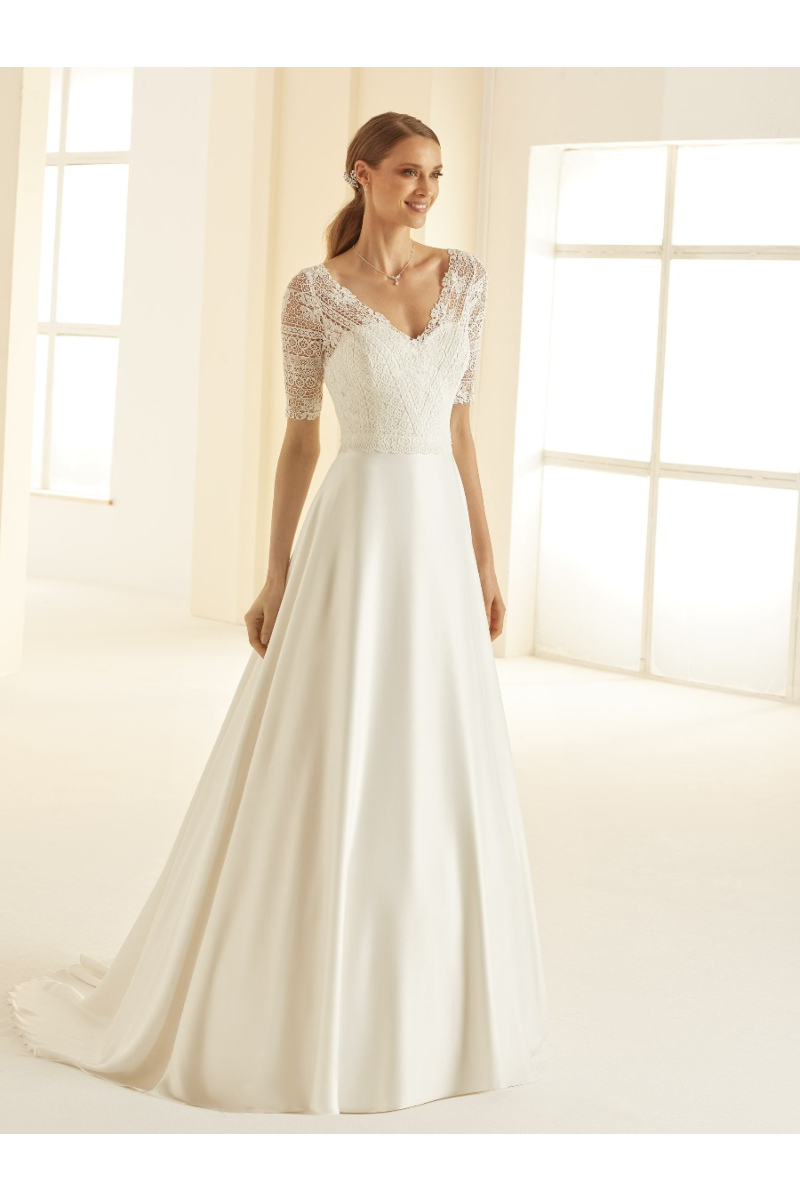 Abito da sposa Barbara con corpetto in pizzo e maniche corte, gonna ampia in seta, ambiente luminoso.