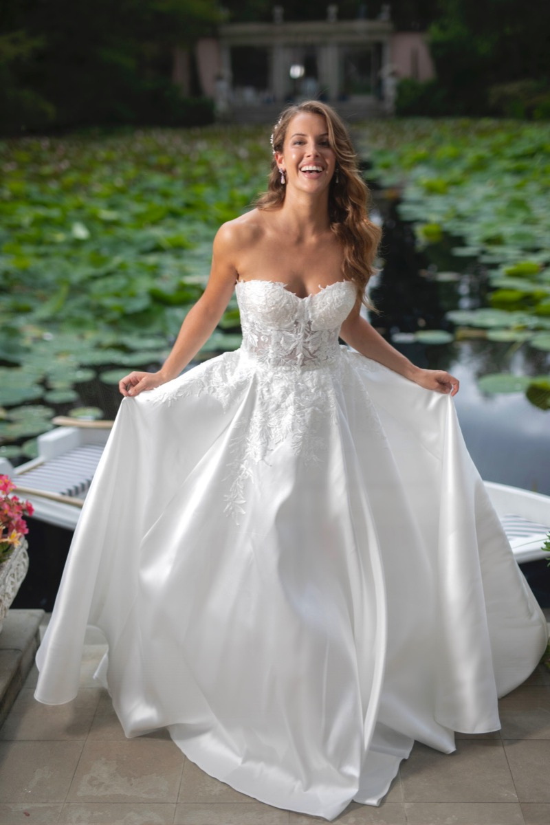 Abito da sposa Afrodite linea Sposae, scollatura a cuore, dettagli in pizzo, sfondo naturale con ninfee.
