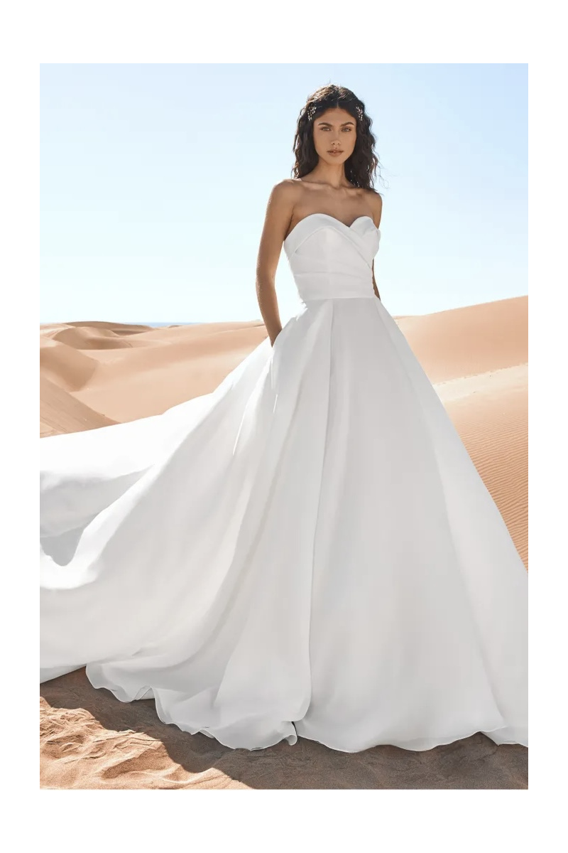 Abito da sposa Pronovias Geiranger in raso bianco, scollatura a cuore, sfondo deserto.
