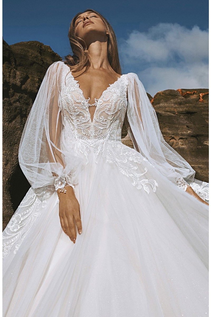 Abito da sposa Pronovias Skye con dettagli in pizzo e maniche trasparenti, sfondo roccioso.
