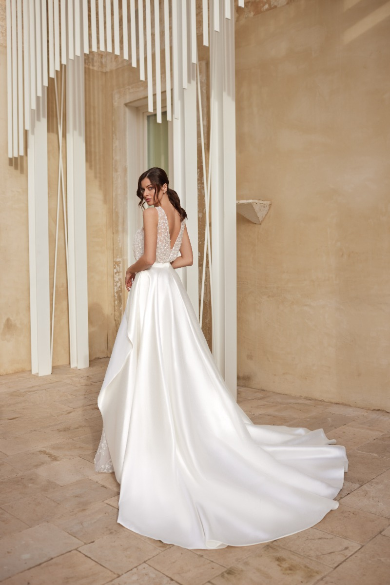 Abito da sposa CRYSTAL di Mark Loren, elegante con schiena scoperta e gonna ampia, ambientazione architettonica moderna.