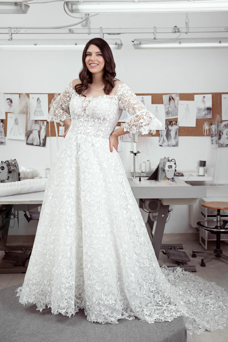 Abito da sposa curvy in pizzo bianco con maniche a tre quarti in atelier sartoriale.