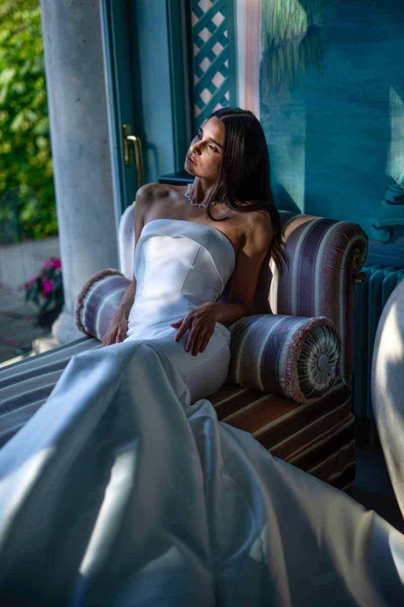 Abito da sposa elegante Arianna linea sposae atelier, donna seduta su divano, ambiente raffinato.