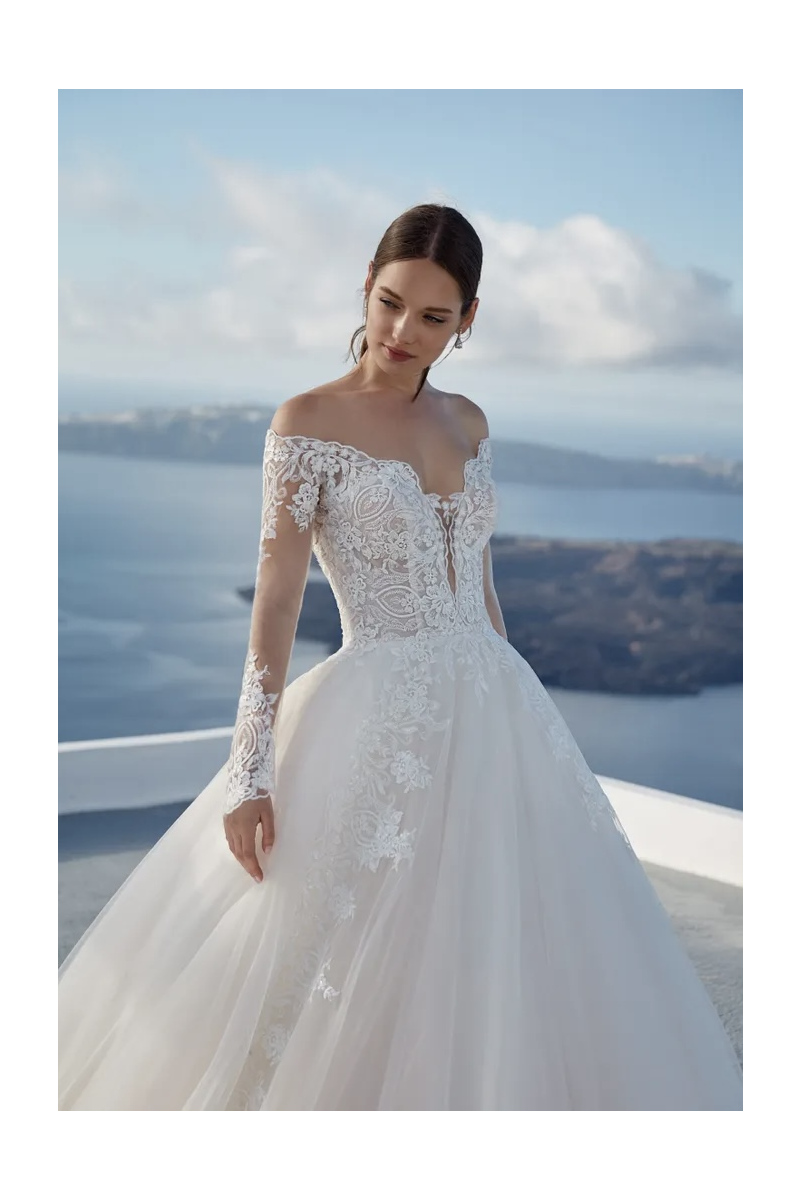 Abito da sposa KAYMAN linea NICOLE Jolies con dettagli in pizzo, sfondo marino suggestivo.