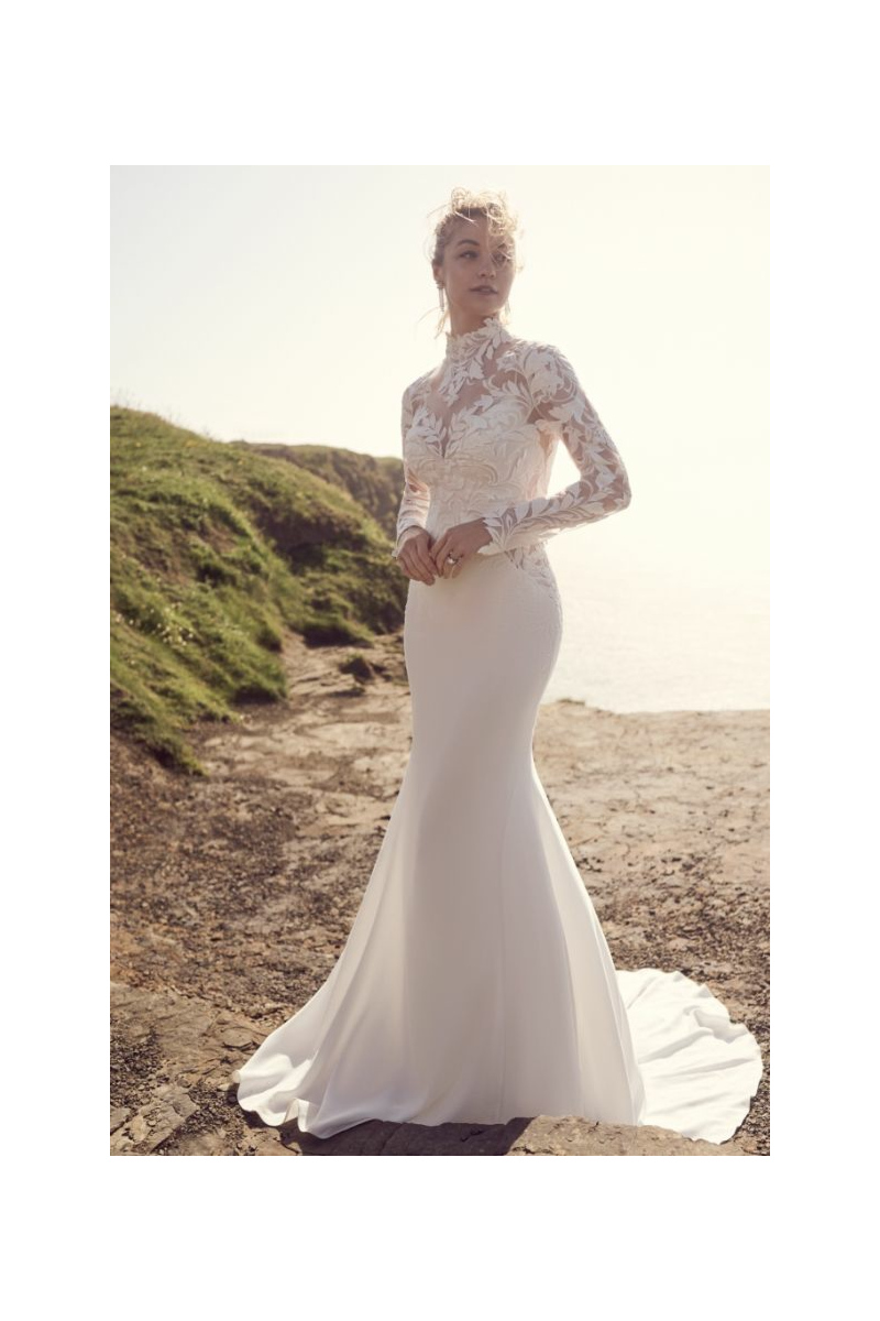 Abito da sposa Dionne Maggie Sottero con pizzo floreale e maniche lunghe, sfondo paesaggio costiero.