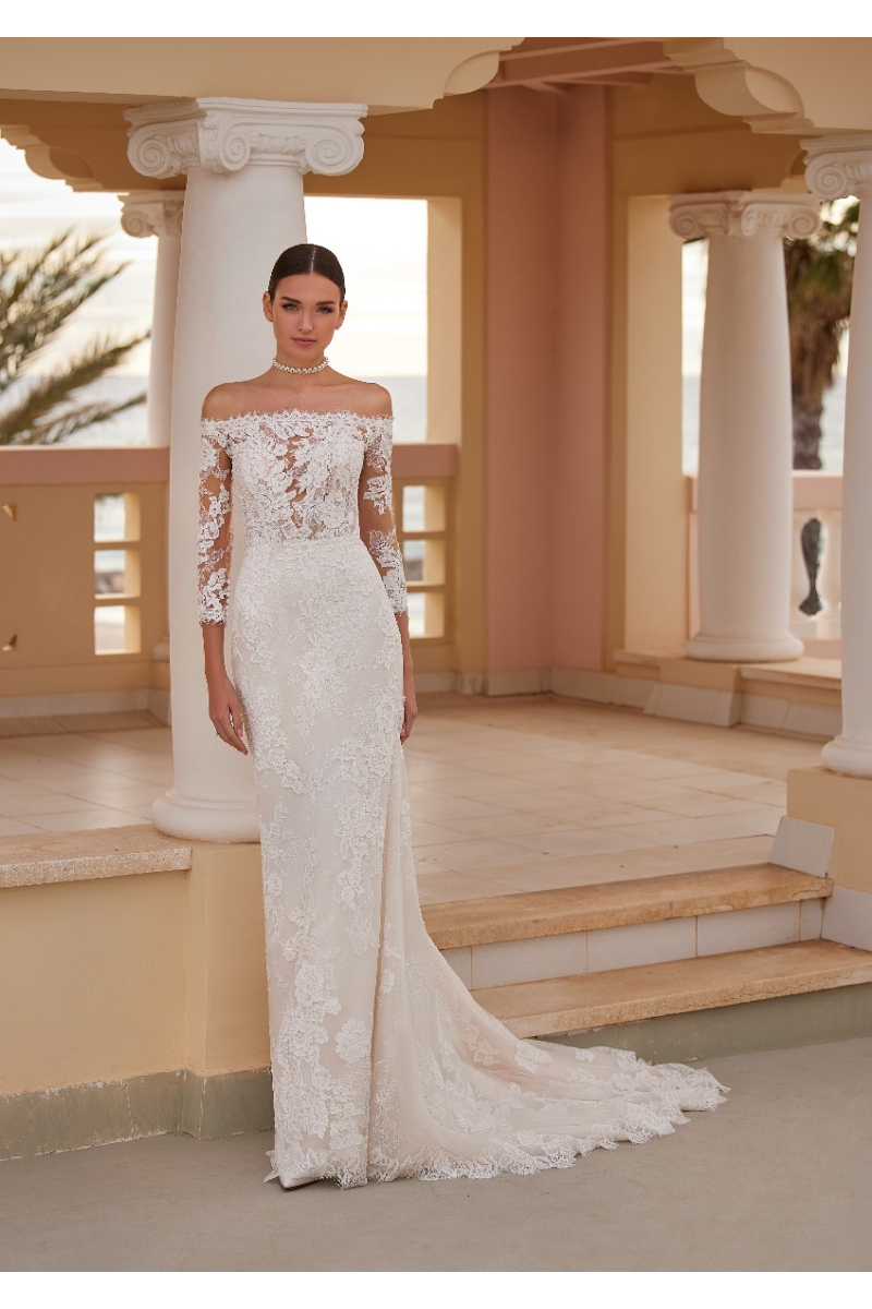 Abito da sposa DORSET in pizzo, spalle scoperte, sfondo architettonico elegante.