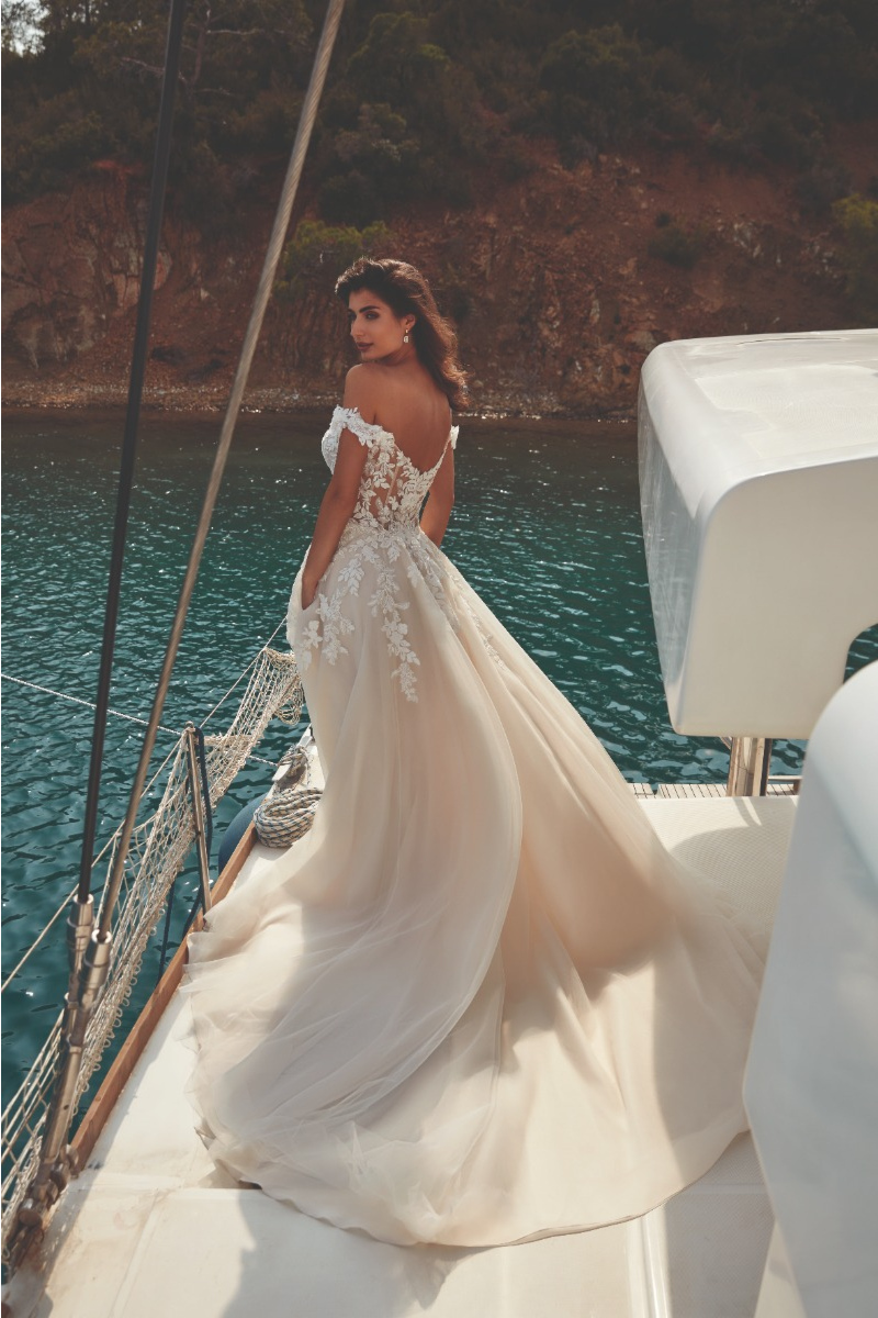 Abito da sposa VANYA di Eddy K su yacht, scollo a cuore e dettagli in pizzo, sfondo mare e scogliera.
