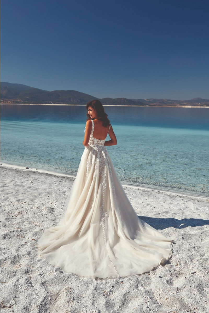 Abito da sposa Eddy K "Samoa" in riva al mare, con dettagli ricamati e sfondo naturale.