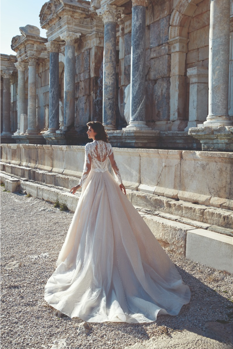 Abito da sposa Eliana di Eddy K con dettagli in pizzo, sfondo con colonne antiche.