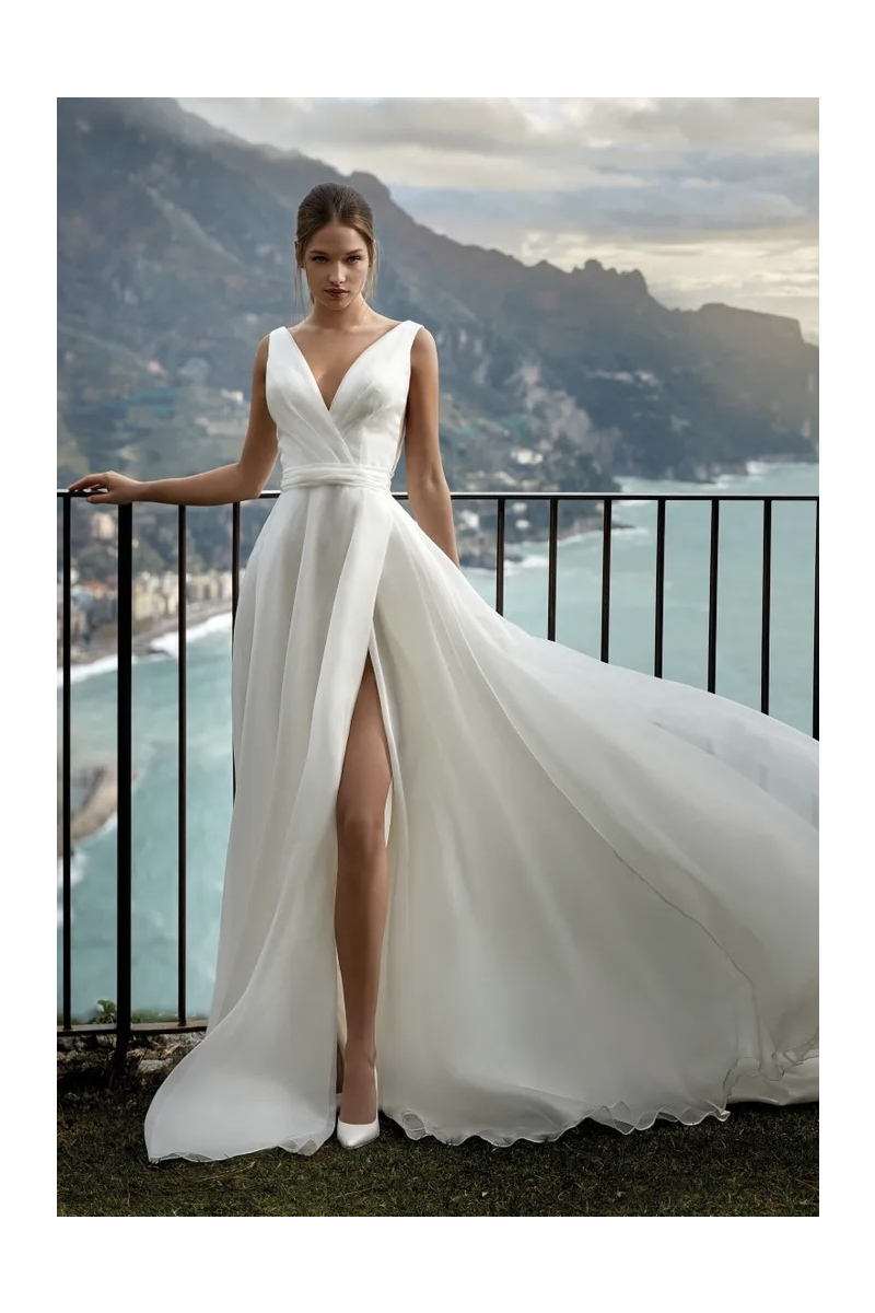 Abito da sposa Gelsey Nicole Jolies, scollo a V, spacco laterale, sfondo costiero.