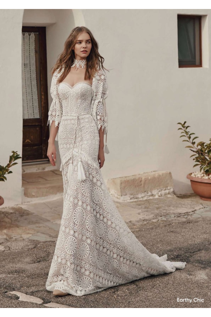Abito boho chic in pizzo bianco con dettagli floreali, stile Earthy Chic, indossato all'aperto.