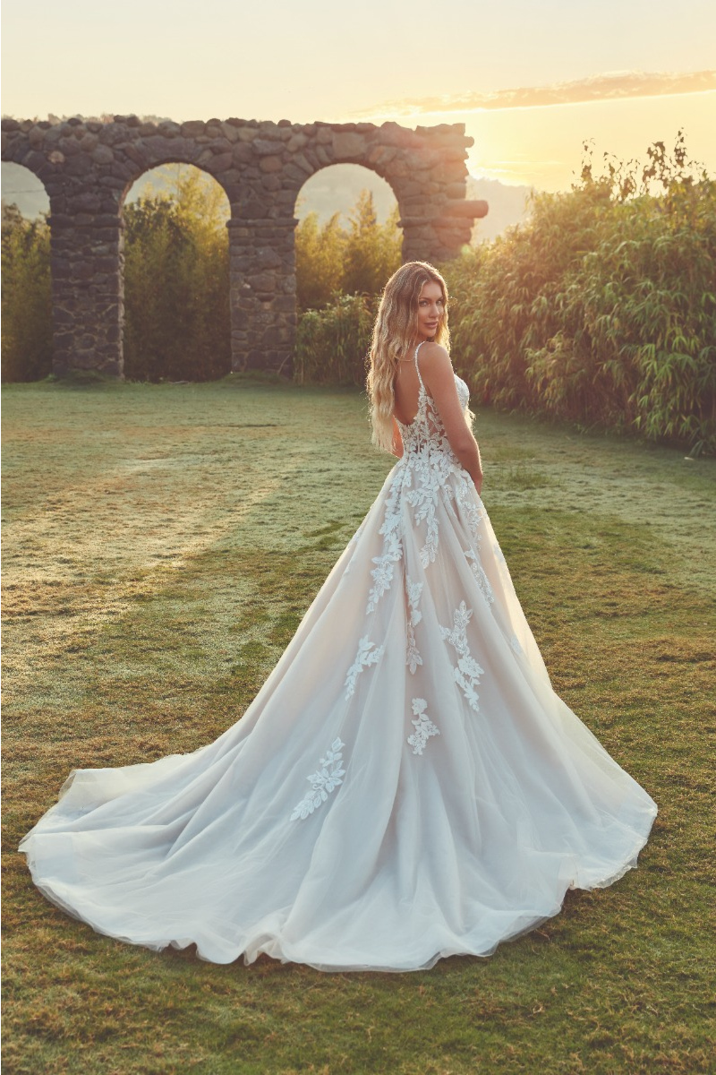 Abito da sposa MACKANZIE di Eddy K, con dettagli floreali, in un giardino al tramonto.
