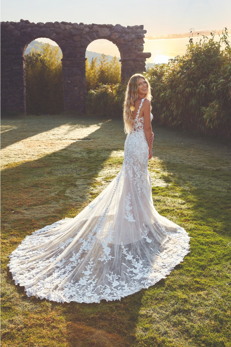 Abito da sposa Carly di Eddy K con strascico in pizzo, ambientato in un giardino al tramonto.