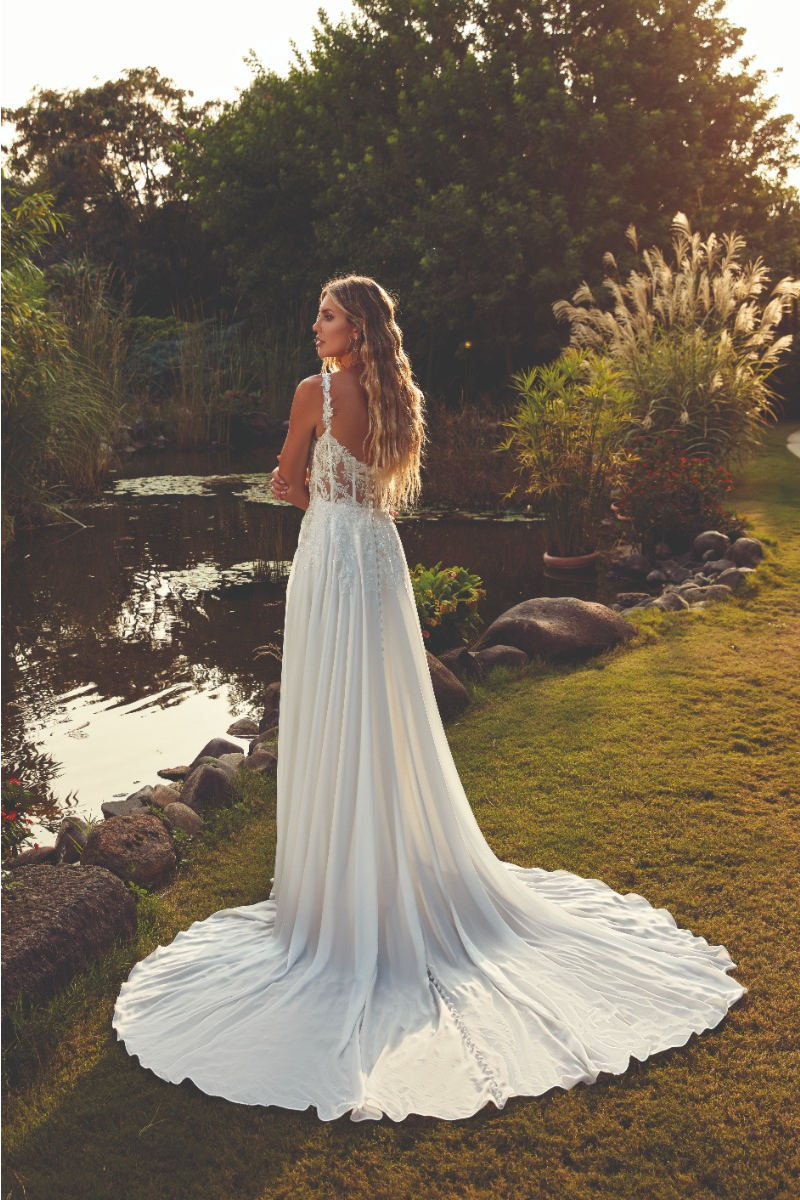 Abito da sposa ROSIE EDDY K con schiena scoperta, lungo strascico, in un giardino al tramonto.